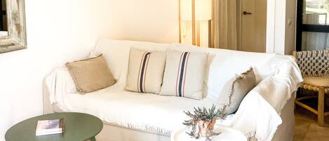 A living room with a white sofa, a small round table, a lamp, and a ceiling fan.