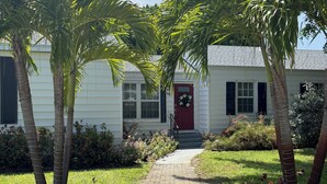 Un sendero conduce a una casa con puerta roja, rodeada de palmeras y un jardín cuidado.