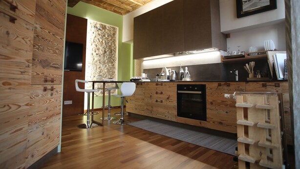 A modern kitchen with wooden cabinetry, a built-in oven, and a bar area with stools. - Epicurus guest house: Zeus (Somma Lombardo)