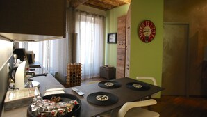 A dining area with a wooden table, chairs, a clock, and a window with curtains. - Epicurus guest house: Zeus (Somma Lombardo)