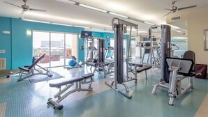 A gym with various exercise machines, large windows, and ceiling fans. - Houston Modern Apt Pool View NRG DISCOUNTED (Houston)