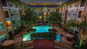 A multi-story hotel with a central pool surrounded by palm trees and outdoor seating areas. - Houston Modern Apt Pool View NRG DISCOUNTED (Houston)
