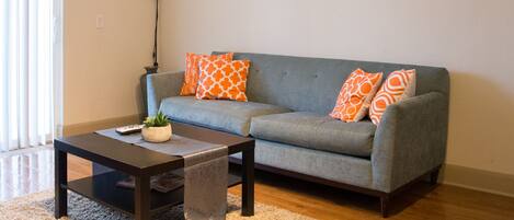 A living room with a gray sofa, orange patterned pillows, a dark coffee table, a white lamp, and a ceiling fan.
