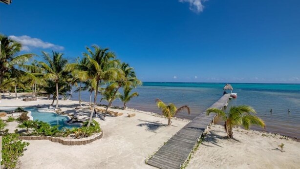 A beach resort with a wooden walkway leading to the water, palm trees, and a pool area. - 606 - 3rd Floor Ocean View Suite (san pedro)