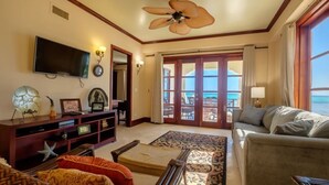 A spacious living room with a large TV, a ceiling fan, and a view of the ocean through the sliding glass doors. - 606 - 3rd Floor Ocean View Suite (san pedro)