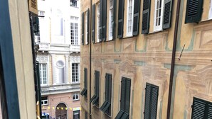Eine schmale Straße mit Gebäuden an beiden Seiten, mit zahlreichen Fenstern und Fensterläden, einem parkenden Auto und einem Motorrad.