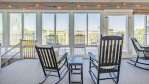 A covered patio with rocking chairs, a table, and string lights. - Luxury Oceanfront Home – Spacious Family Retreat Steps from the Beach (Tybee Island)