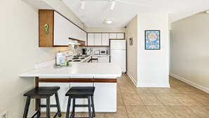 A modern kitchen with white cabinetry, a central island with stools, and a seahorse decoration on the wall. - Emerald Skye 54 (Orange Beach)