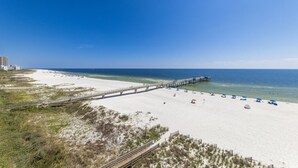 A beach with a pier extending into the ocean, sandy beach, and a clear blue sky. - Emerald Skye 54 (Orange Beach)