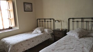 A room with two single beds with floral bedding, a nightstand with a lamp, and a window with blinds. - TREASURE HOUSE IN RESERVE OF THE BIOSPHERE PICOS DE EUROPA (Cangas de Onís)