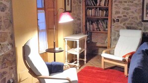 A cozy living room with a stone wall, a bookshelf, a white armchair, a red rug, and a floor lamp. - TREASURE HOUSE IN RESERVE OF THE BIOSPHERE PICOS DE EUROPA (Cangas de Onís)