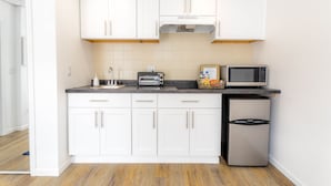 Cozinha compacta com armários brancos, micro-ondas, torradeira e geladeira.