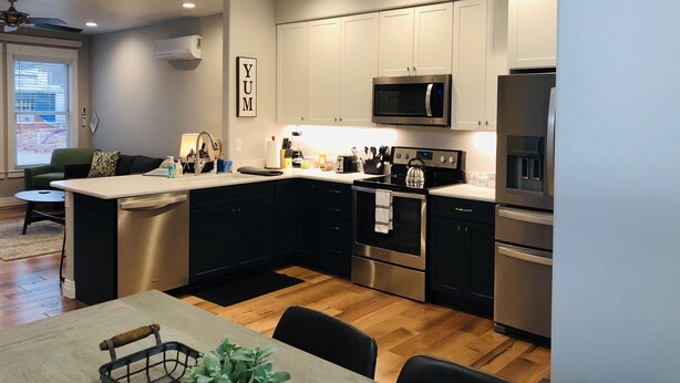 A modern kitchen with stainless steel appliances, a dining area with a wooden table, and a view of the city through a large window. - New Luxury Condo in Downtown Salida #0677 (Salida)