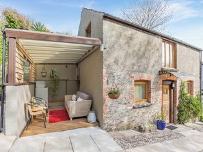 Un charmant cottage doté d’un porche abrité, d’un petit coin salon et d’une façade en pierre rustique.