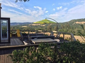 Terraza exterior con sofá, sillas y una mesa, con vistas a un paisaje montañoso.
