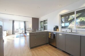 A modern kitchen with a central island, a built-in oven, and a large window overlooking a natural landscape.