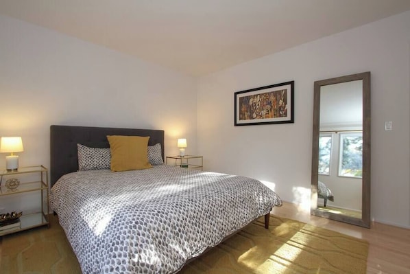 A bedroom with a bed, bedside lamps, a framed artwork, and a mirror.