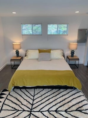 A bedroom with a bed, two bedside tables, two lamps, a window, and a patterned rug.
