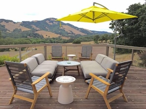 A deck with a sofa set, two chairs, a small table, and a yellow umbrella.