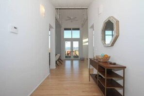 A hallway with a wooden floor, a ceiling fan, a wall-mounted mirror, and a view through a glass door to the outside. - Modern Panoramic Hillside Escape (Santa Rosa)