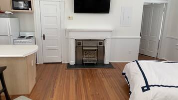 A compact room with a white fireplace, a flat-screen TV mounted above it, a microwave on a shelf, and a stove in the corner.