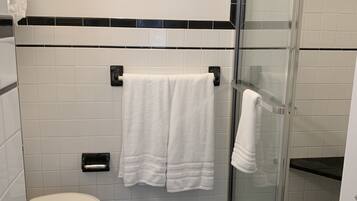 A bathroom with a toilet, two white towels hanging on a rack, a glass shower enclosure, and a black and white checkered floor pattern.