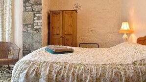 A bedroom with a bed, a wooden wardrobe, a lamp, and a wicker chair.