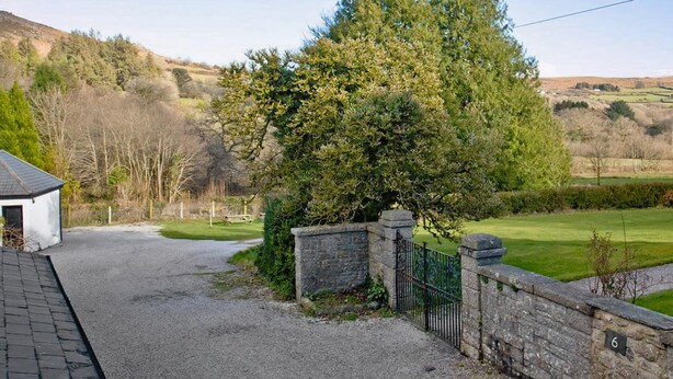 A rural property with a gravel driveway leading to a stone wall and a small white building.