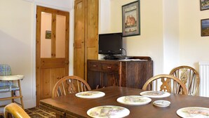 A dining room with a wooden table set for four, a television on a wooden cabinet, and a chair with a decorative backrest.