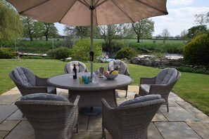 A round outdoor table with wicker chairs, a large umbrella, and a bowl of fruit. - Riverside House, Bidford-on-Avon, Stratford-upon-Avon (Bidford-on-Avon)