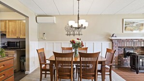 A dining area with a wooden table and chairs, a chandelier, and a fireplace. - Lodge Condo 24 (Stowe)