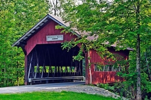 A red covered bridge named Brockdale Bridge with a sign, surrounded by lush green trees. - Lodge Condo 24 (Stowe)