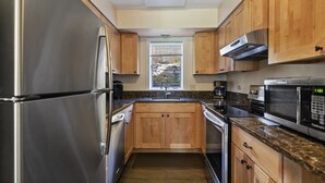A compact kitchen with stainless steel appliances, wooden cabinets, and a window providing a view of the outdoors. - Lodge Condo 24 (Stowe)