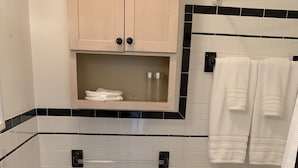 Een badkamer met toilet, wastafel en bad. Handdoeken hangen aan een rek en boven het toilet bevindt zich een kast.