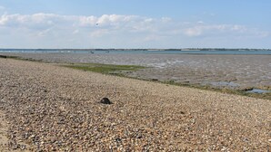 A pebbled beach with boats in the water and a distant shoreline. - 2 bedroom accommodation in St. Lawrence, near Burnham-on-Crouch (St. Lawrence, near Burnham-on-Crouch)