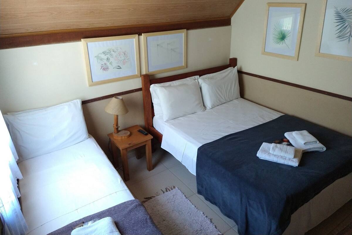 Ein Schlafzimmer mit zwei Betten, einem Nachttisch mit Lampe und gerahmten Bildern an der Wand.