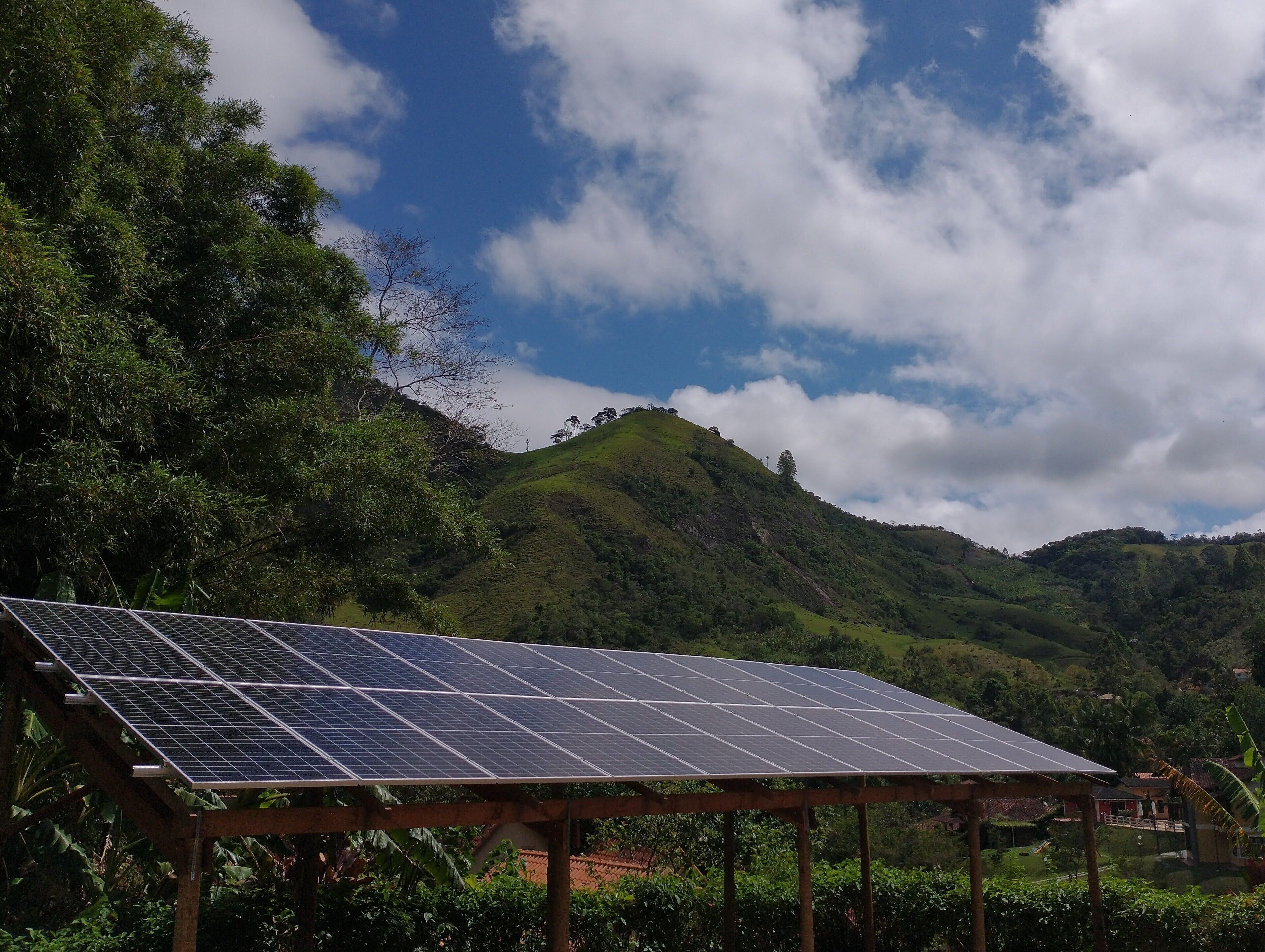 A solar panel installation on a wooden structure with a view of green hills and a partly cloudy sky.