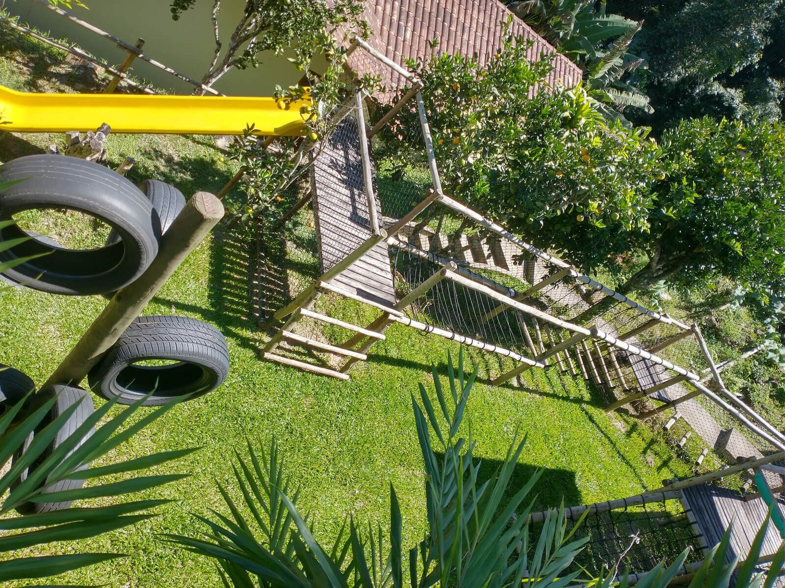 Un parque infantil con una estructura de madera para escalar, columpios de neumático y un tobogán amarillo.