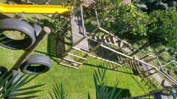 Un parque infantil con una estructura de madera para escalar, columpios de neumático y un tobogán amarillo.