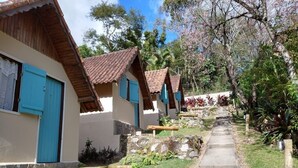 A row of traditional-style cottages with tiled roofs and blue shutters, a stone pathway, and lush greenery. - Pousada dos Anjos (Nova Friburgo)