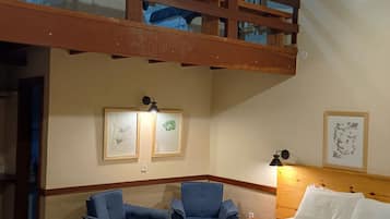 A room with a bunk bed, two chairs, a bedside table, and artwork on the walls.