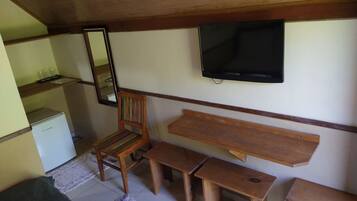 A small, cozy room with a wooden ceiling, a television mounted on the wall, a wooden chair, a small table, and a bench.