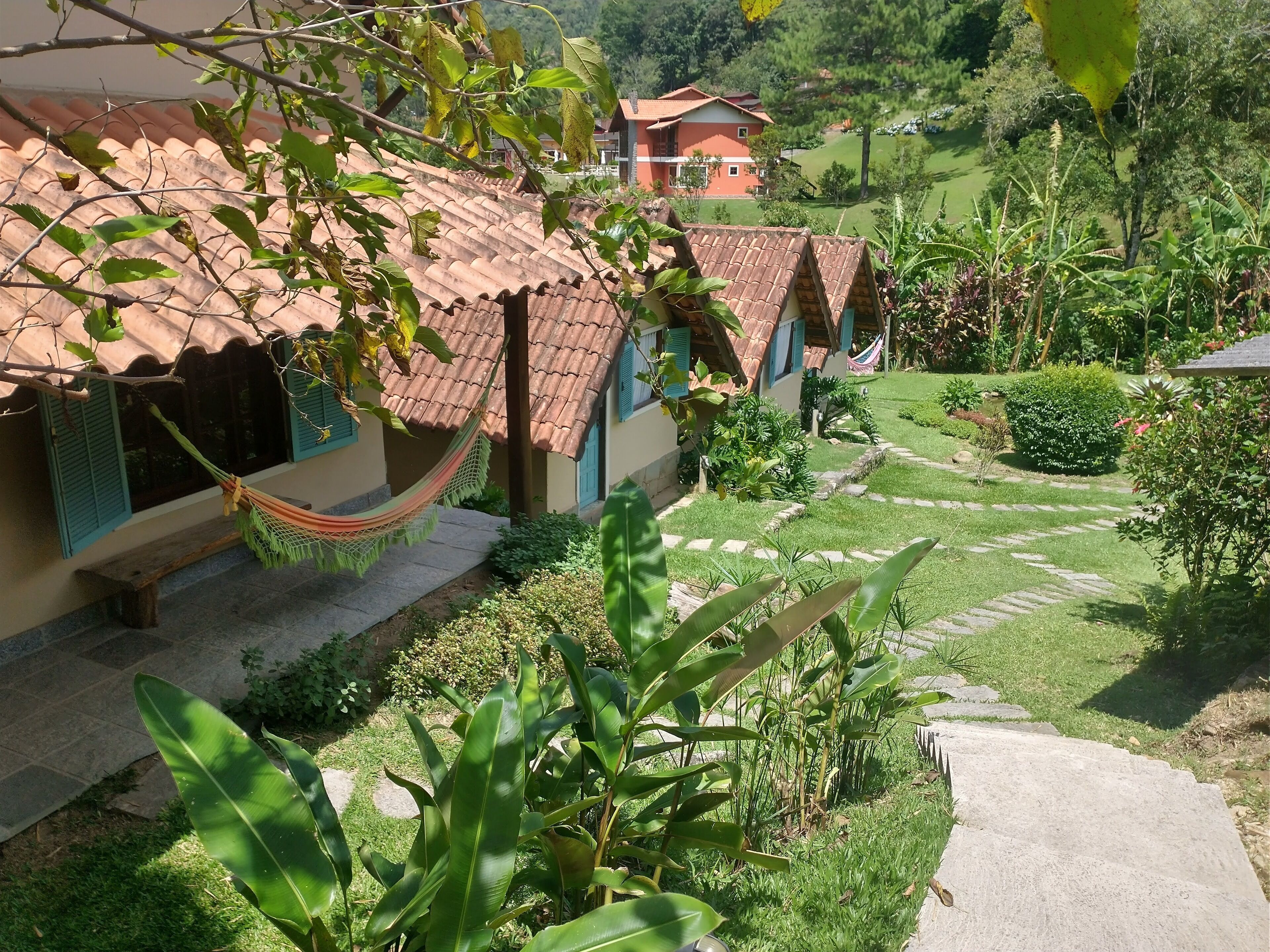 Un bâtiment doté d’un toit en tuiles, d’un hamac et d’un jardin bien entretenu avec un chemin en pierre.