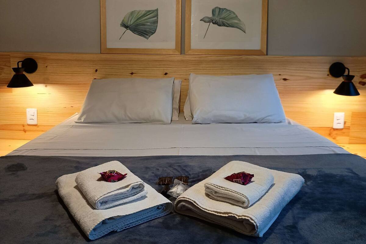 Ein ordentlich gemachtes Bett mit zwei Kissen, einem Kopfstück mit gerahmten Pflanzenbildern und zwei Nachttischlampen.
