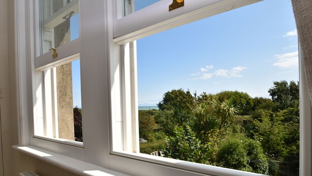 Ein Fenster mit Blick auf einen üppigen Garten und eine ferne Landschaft.