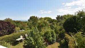 Ein üppiger Garten mit verschiedenen Pflanzen und Bäumen, einer hölzernen Bank und Blick aufs Meer.