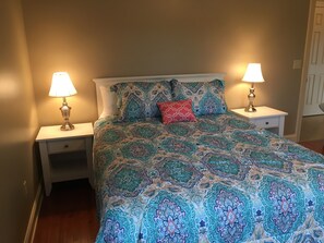 A bedroom with a patterned bedspread, two bedside lamps, a nightstand with a drawer, and a door in the background. - Beautiful Getaway amazing views! Sleeps 6 (Dushore)