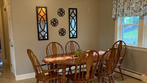 Un coin repas avec une table ronde, six chaises en bois et un ventilateur de plafond.