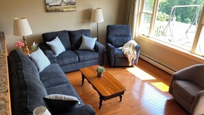 Un salon avec un canapé, des fauteuils, une table basse en bois et un tableau accroché au mur.