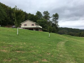 A house on a grassy hill with a white fence and a red car parked nearby. - Beautiful Getaway amazing views! Sleeps 6 (Dushore)